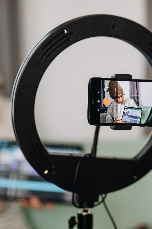Smartphone filming a presenter through a ring light as part of remote corporate video services setup.